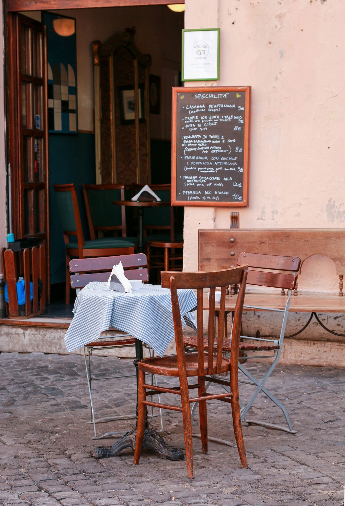 Scaun bistro din lemn la o masă de cafenea, pe o stradă pavată, în fața unui restaurant