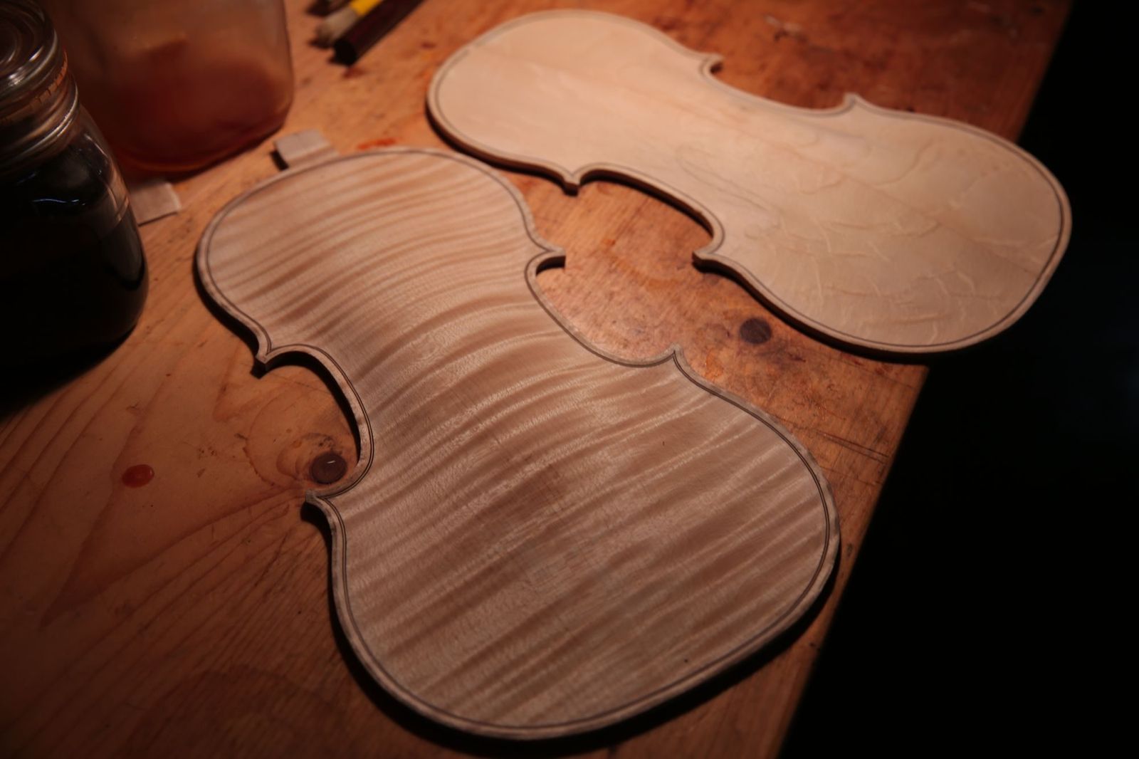 Unvarnished violin plates on a luthier's workbench, the front one a flamed maple back