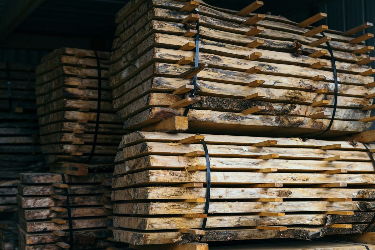 Bundles of live-edge boards, stickered and strapped, stacked to dry under a roof