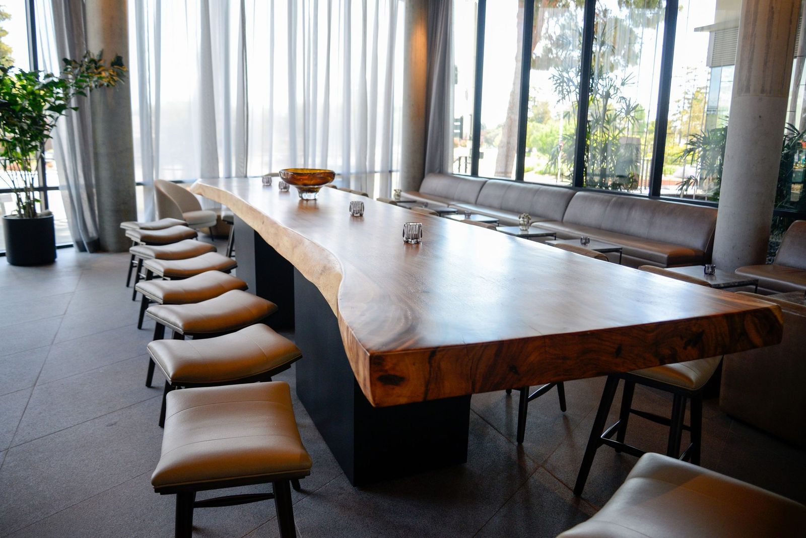 Long live-edge slab table with leather bar stools in a bright restaurant