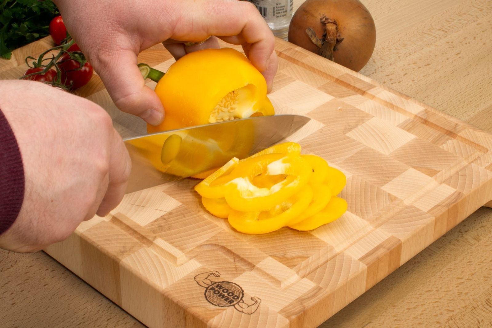 Manos cortando un pimiento amarillo con un cuchillo de chef sobre una tabla de cortar de testa de haya con dibujo de damero