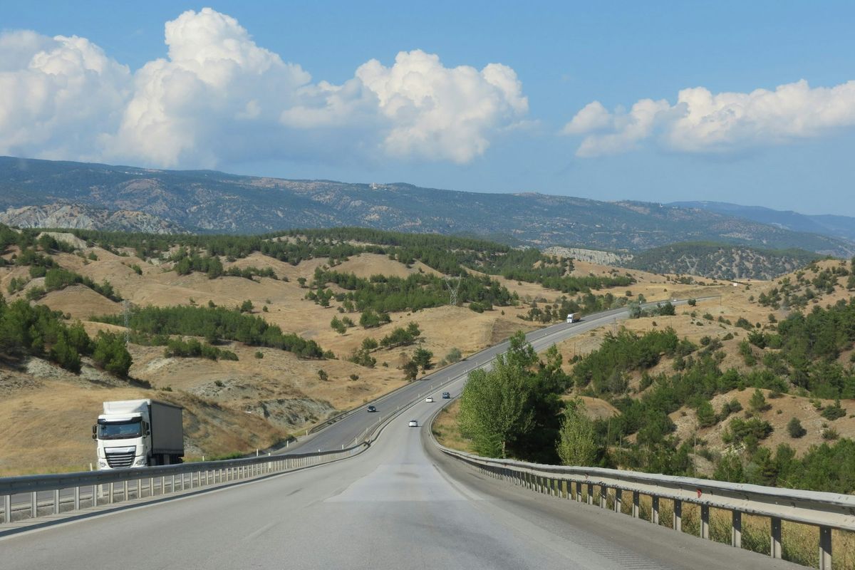 Poids lourd sur une autoroute à deux chaussées serpentant entre des collines sèches et boisées