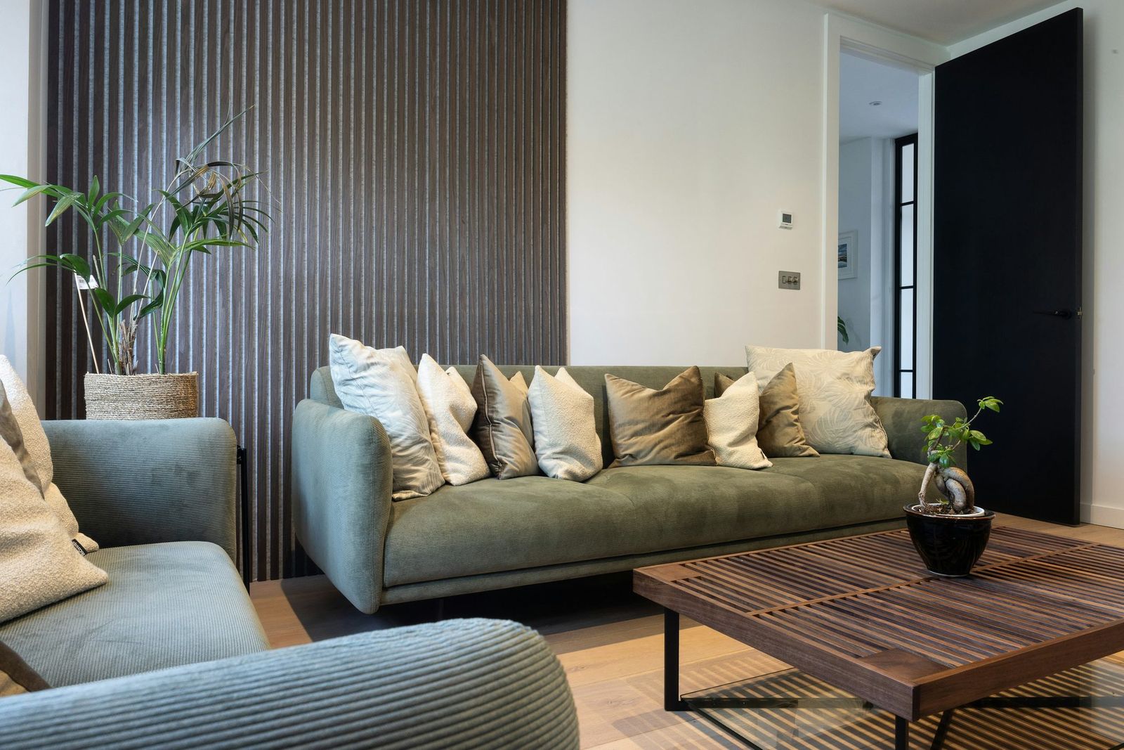 Living room with a dark wood slat wall behind a green sofa and a coffee table
