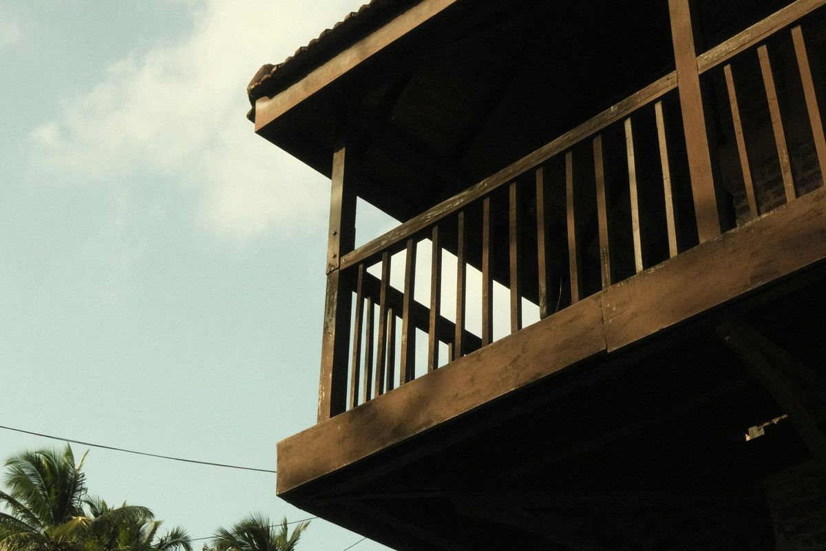Balustradă de balcon din lemn cu baluștri verticali, văzută de jos, pe fundalul cerului